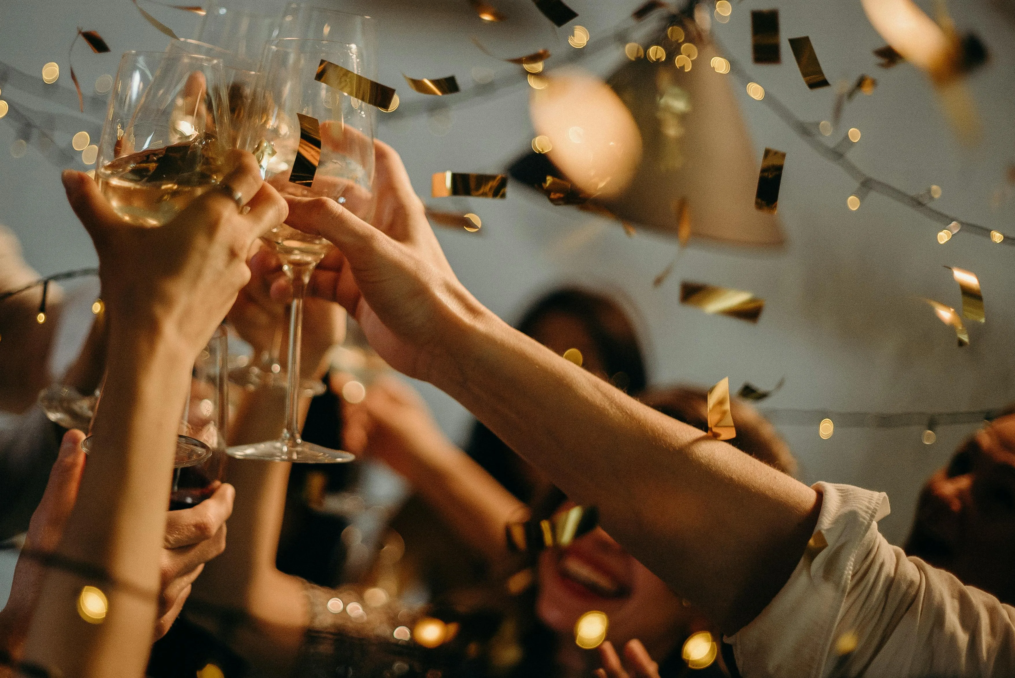 Mains levées trinquant avec des coupes de champagne sous une pluie de confettis dorés