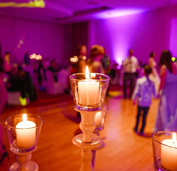 Bougies dans des photophores en verre au premier plan d'une salle de réception éclairée en violet avec des invités en arrière-plan